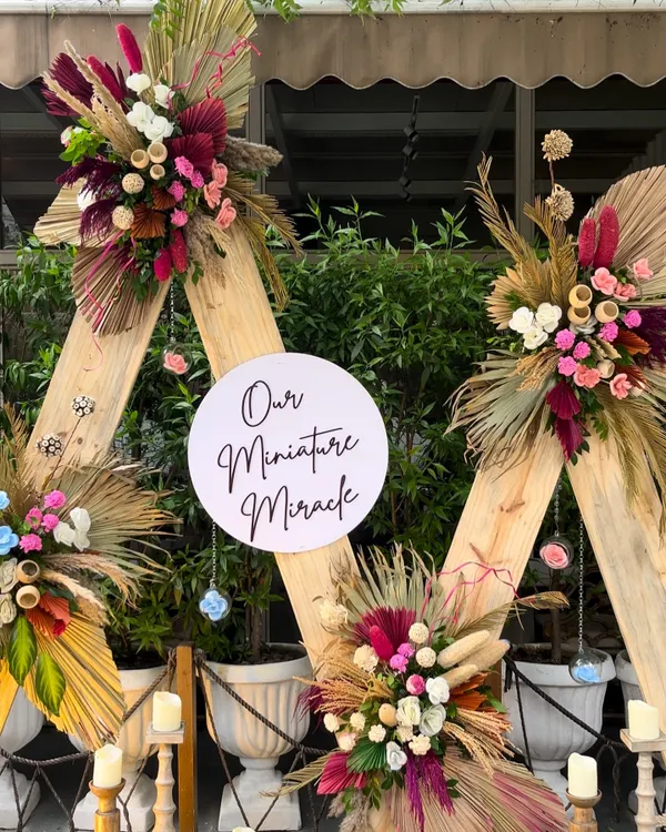 A stunning boho-chic baby shower backdrop. We used triangular wooden frames adorned with vibrant dried florals, pampas grass, and a sign celebrating "Our Miniature Miracle."