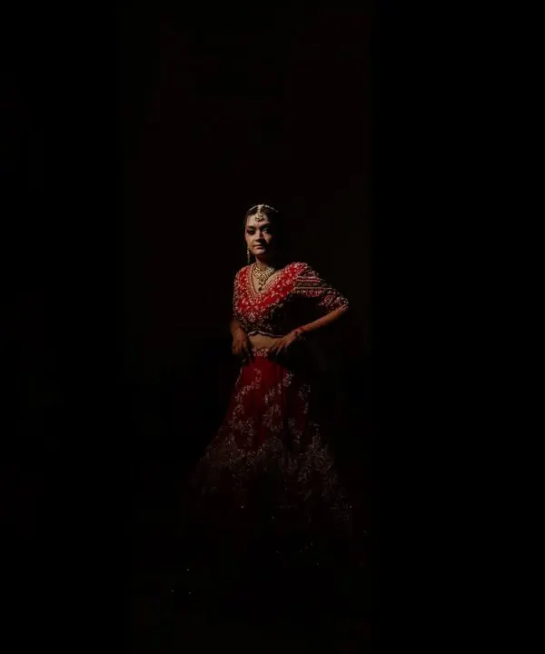 A dramatic and artistic bridal portrait of Anjali. The use of shadow and light creates a powerful image that highlights her beauty and the richness of her red lehenga.