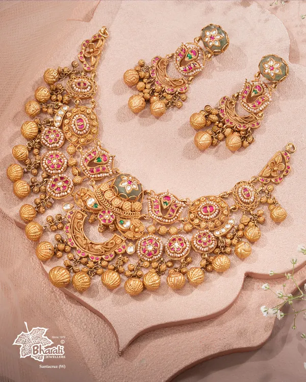 A legacy that adorns generations. This heritage bridal necklace, with its intricate patterns, ruby and emerald-hued stones, and clusters of golden ghungroos, is handcrafted to tell your story in gold and grace. It is an heirloom in the making.
