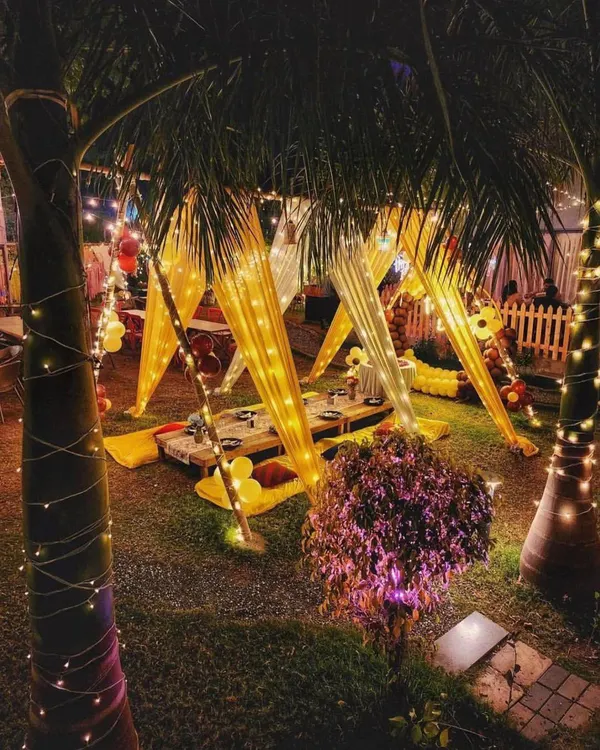 A beautiful nighttime view of a garden party setup, with canopy tents illuminated by fairy lights, creating a warm and inviting atmosphere.