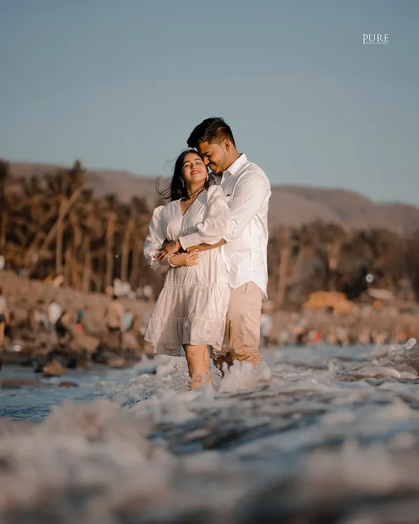 Komal and Ajit share a tender embrace while standing in the gentle waves of the sea. The warm golden hour light makes this beach pre-wedding photo incredibly romantic.