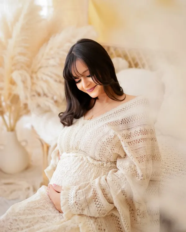 A portrait capturing the quiet joy and anticipation of motherhood. This mama-to-be is glowing in a soft, cream-colored knit dress, surrounded by a dreamy, light-filled boho setup in my studio.