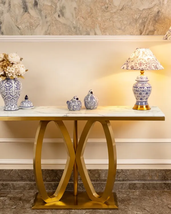 This console table features a white marble top and a striking gold stainless steel base with an interlocking oval design. It's a glamorous and modern piece, perfect for an entryway or living room.