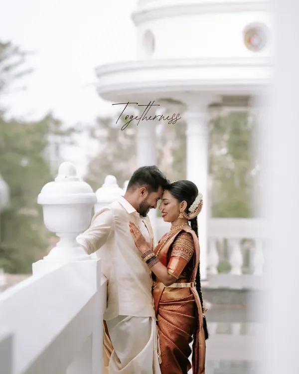 A quiet moment of togetherness captured against a classic white colonnade. We focus on capturing the gentle connection between two souls, preserving the authentic feeling of your wedding day in our South Indian wedding photography.