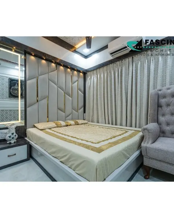 A luxurious master bedroom in Jogeshwari featuring a floor-to-ceiling upholstered headboard with geometric gold inlay. The backlit vanity mirror and plush wingback chair add to the room's sophisticated and comfortable feel.