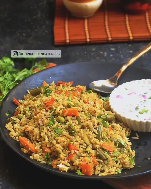 Our Vangibath is a flavorful and aromatic rice preparation from Karnataka, made with eggplant, a special spice powder, and fresh vegetables. It is served here with a cooling side of vegetable raita.