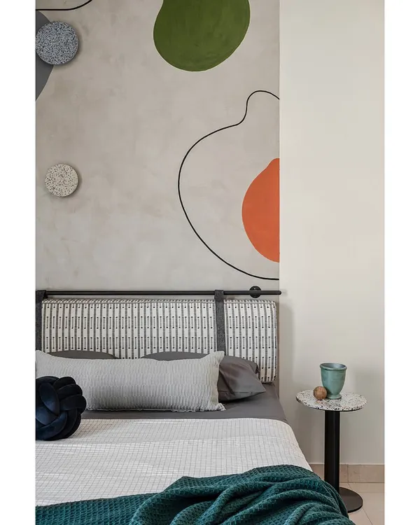 The headboard in this kids' room is set against a hand-painted abstract mural that adds a splash of color and whimsy. Terrazzo accents on the side table and lights introduce texture and fun.