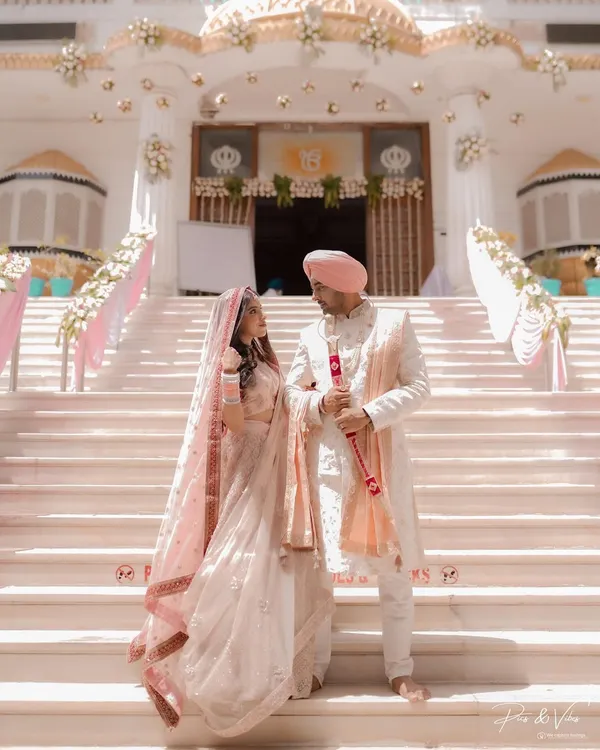 A majestic portrait of a Sikh couple on the steps of the Gurudwara. Their pastel pink outfits are the picture of elegance against the grand white architecture.
