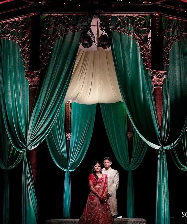 A grand, dramatic portrait of a couple standing amidst elegant green drapes. This shot highlights the beautiful decor and creates a regal, cinematic feel for their pre-wedding shoot.