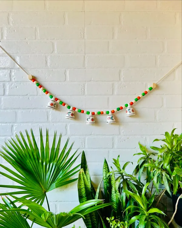 Our 'Khanak' beaded bell bunting in a festive red and green combination. This 30-inch wide bunting features five delicate mini ceramic bells and colorful wooden beads, perfect for adding charm to your entrance or temple space.