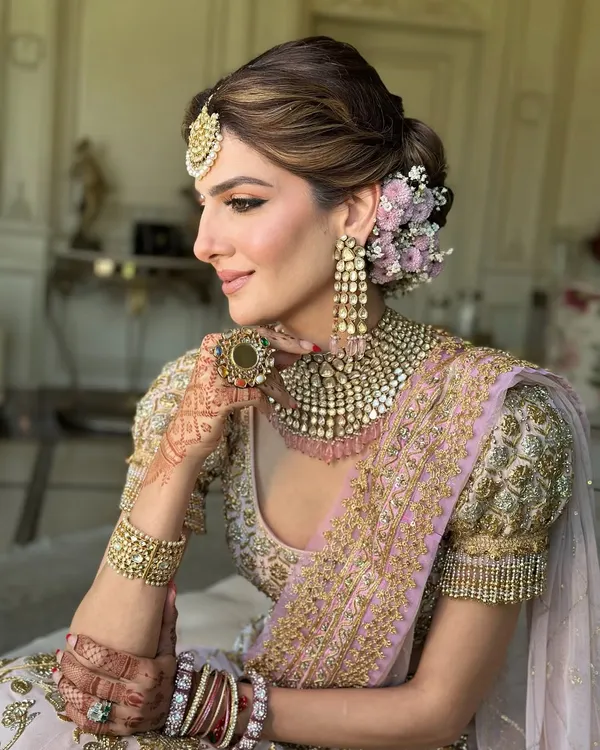 A classic bridal look featuring a soft, textured low bun. I adorned this updo with a semi-circle of fresh pink and white flowers to match the bride's pastel lehenga, creating a look of pure elegance.