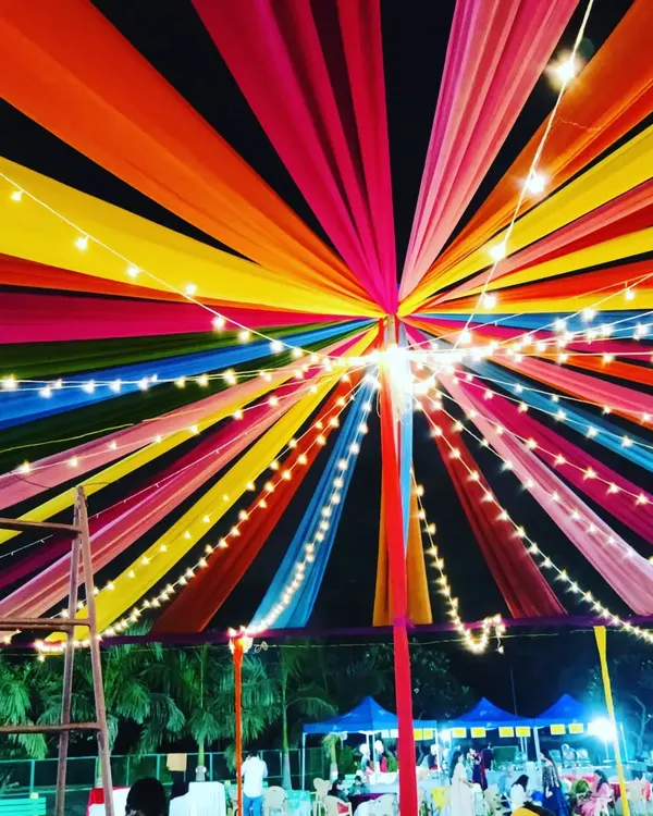 A close-up view from underneath the massive Dandiya night canopy. The radiating strips of colorful fabric are interwoven with bright string lights, showing the detailed craftsmanship that goes into our large-scale festive decorations.