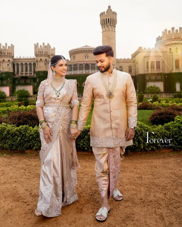 A fairytale moment at the Bangalore Palace. The groom's cream sherwani with a subtly contrasting pastel pink dhoti and stole was designed to match the delicate, intricate embroidery on the bride's breathtaking saree.