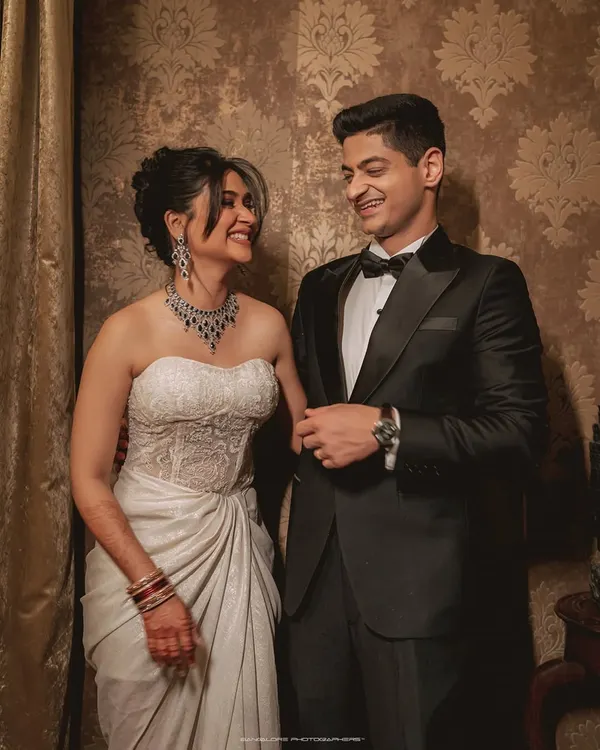 A beautiful, classic portrait of a couple in formal evening wear. Their shared glance and smiles speak volumes, captured against an elegant, patterned backdrop at Villa Kasu.