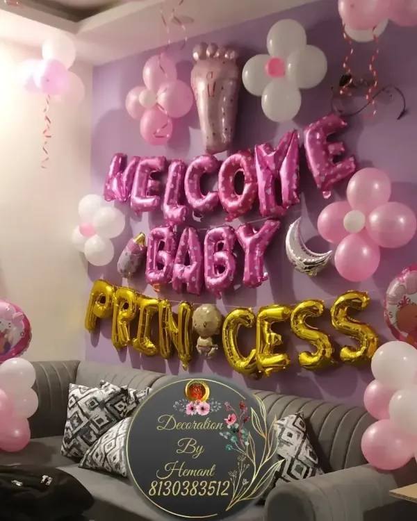 A "Welcome Baby Princess" decoration for a home celebration. The wall is decorated with pink and white balloons, flower-shaped balloon clusters, and large foil letters spelling out the welcome message.