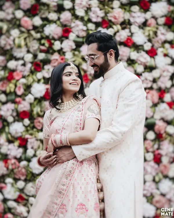 A beautiful portrait of a couple in coordinated pastel outfits against a floral backdrop. This image is all about elegance, showcasing the intricate details of their traditional wear and their loving gaze.
