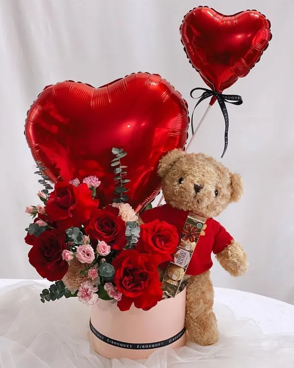 A classic Valentine's Day gift. This hamper comes with a teddy bear holding a bar of chocolate, a box of red roses, and heart shaped foil balloons.