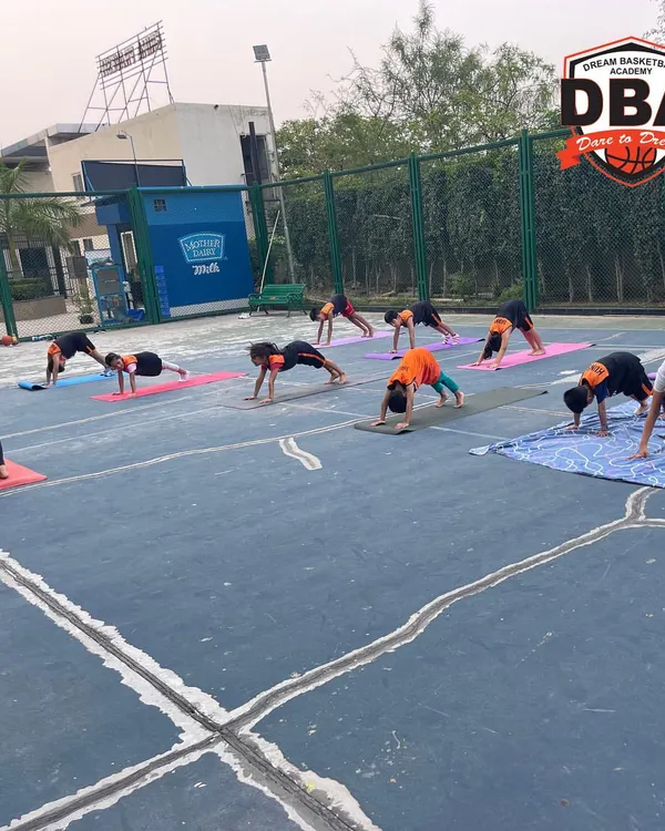Our students practicing the downward dog pose during an outdoor yoga session. This helps improve flexibility in the hamstrings and shoulders, crucial for basketball players.