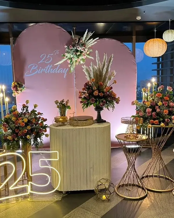 I designed this sophisticated setup for a 25th birthday, combining soft pink backdrops with lush floral arrangements and modern neon lighting. This shows how I create elegant and memorable atmospheres for adult milestone celebrations.