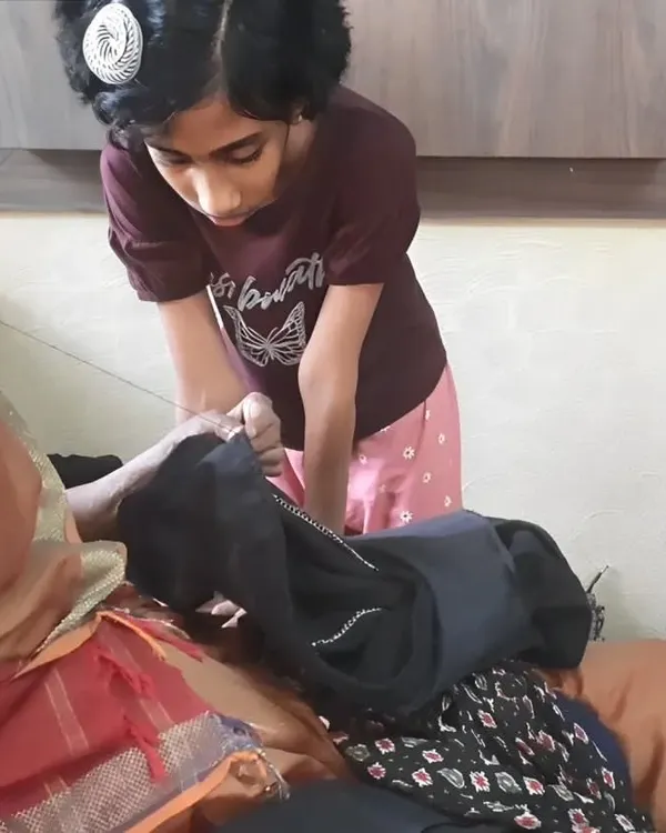 An older family member passes down the skill of sewing to a young girl. We believe in intergenerational learning and the value of preserving traditional repair skills like mending clothes.