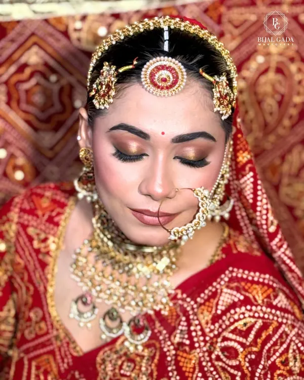 A close-up of the Marwadi bridal makeup, focusing on the golden-bronze eyeshadow that complements the red 'borla' and intricate nath. The look is all about rich colors and flawless skin.