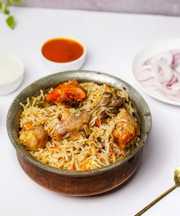 A traditional handi of chicken biryani, served with raita, chutney, and onions on a clean white background, perfect for menus.