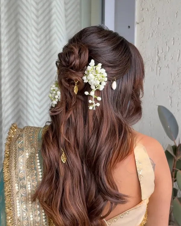 A beautiful half-updo for a baby shower, featuring a messy floral bun with fresh mogra and delicate gold leaf charms hanging from the waves.
