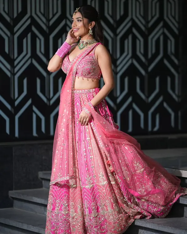 A vision in pink. This look pairs a beautifully embroidered pink lehenga with a statement choker featuring a large green stone and sparkling zircons, perfect for a sangeet or reception.