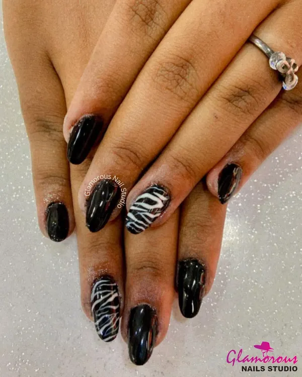 A walk on the wild side. This edgy design features a glossy black polish with accent nails showcasing a classic black and white zebra print.