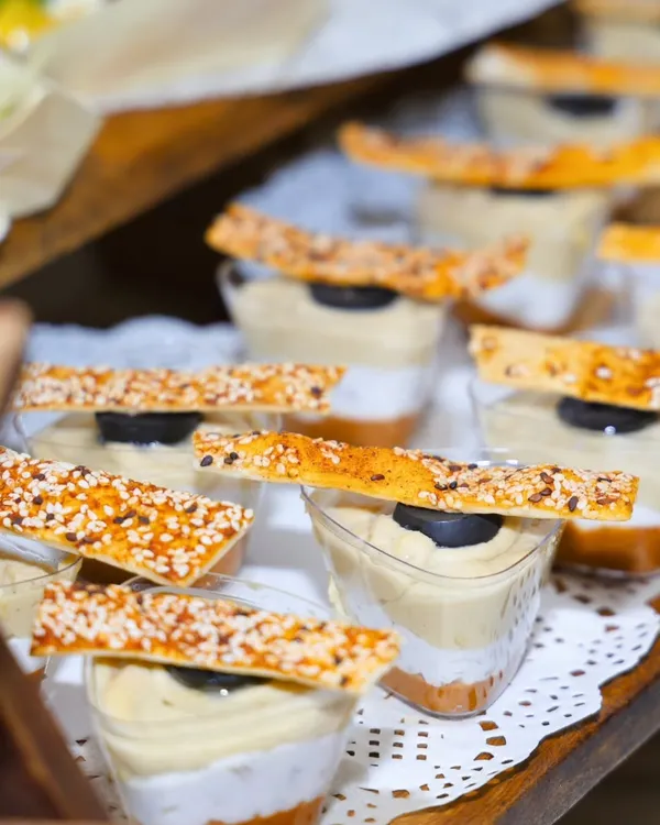 A close-up of our layered hummus dessert cups, topped with a sesame cracker. This dish is a celebration of creativity, where we blend flavors from across continents and serve memories that are thoughtfully presented.