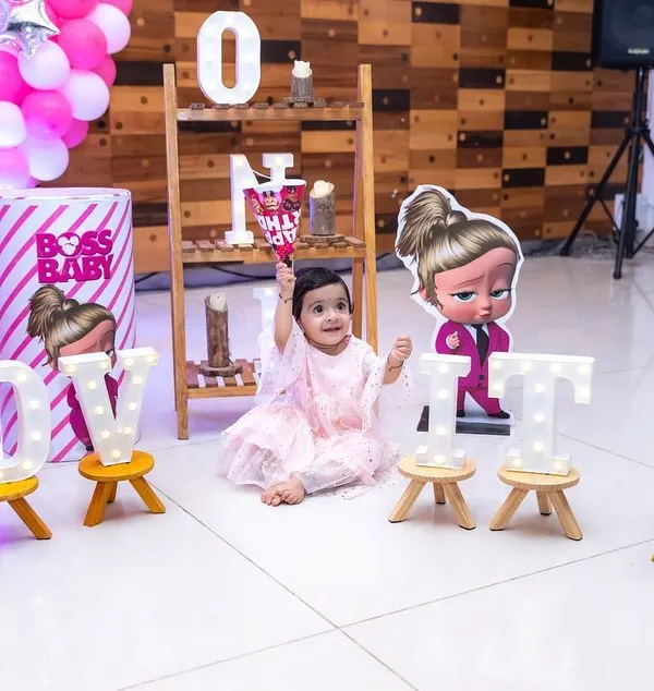 A one-year-old girl sits amidst her 'Boss Baby' themed birthday decorations, complete with marquee lights spelling her name. We excel at capturing solo portraits of the birthday star within their party setup.