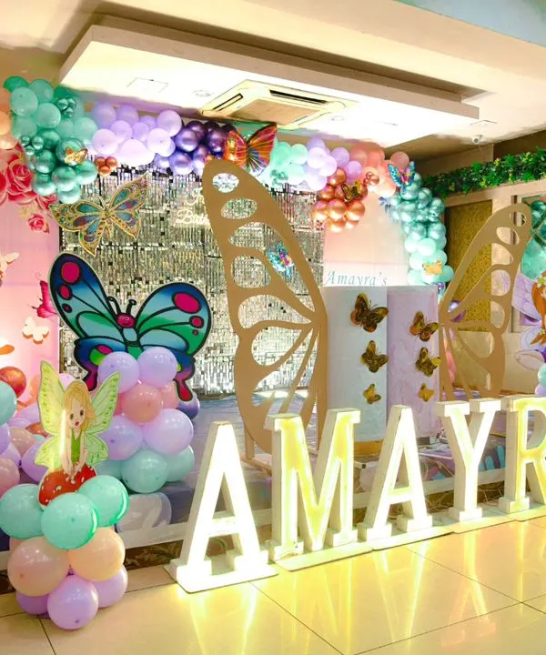 A wide view of our elaborate Butterfly Garden birthday setup. It features a stage with illuminated letters, large wooden butterfly wings, fairy cutouts, and extensive balloon sculptures in pastel shades.