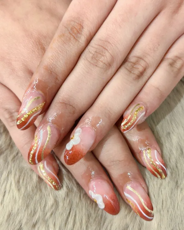 A warm and elegant design featuring a burnt orange ombre effect, accented with delicate white and shimmering gold waves. This is a perfect example of a sophisticated, artistic nail set.