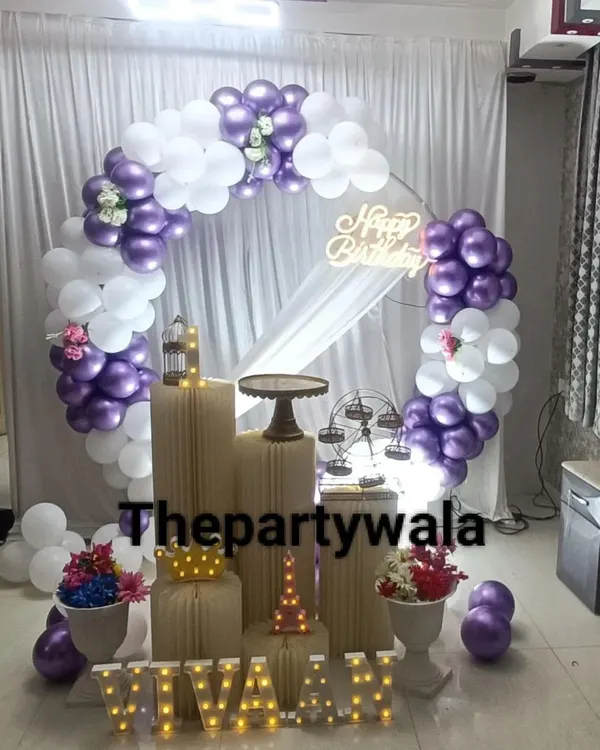 A chic ring decoration with purple and white balloons, a sheer white curtain, and light-up letters for the name 'VIVAAN'.