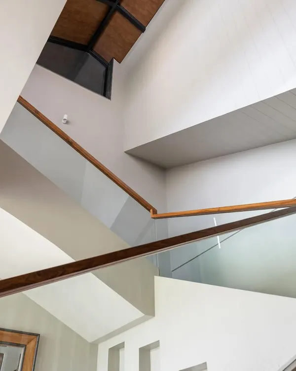 The double-height staircase in Grove House creates a sense of spaciousness and light. The clean lines of the glass and wood railing are a modern counterpoint to the home's tropical setting.