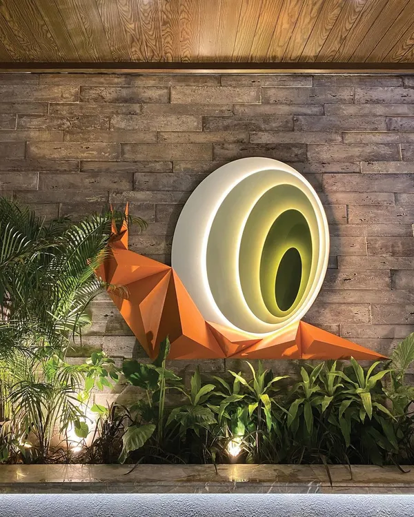 This biophilic snail art installation, titled 'Harmony in Motion,' is nestled within a landscaped court. The origami-like form and internal lighting create a captivating sense of wonder and tranquility, especially at night.