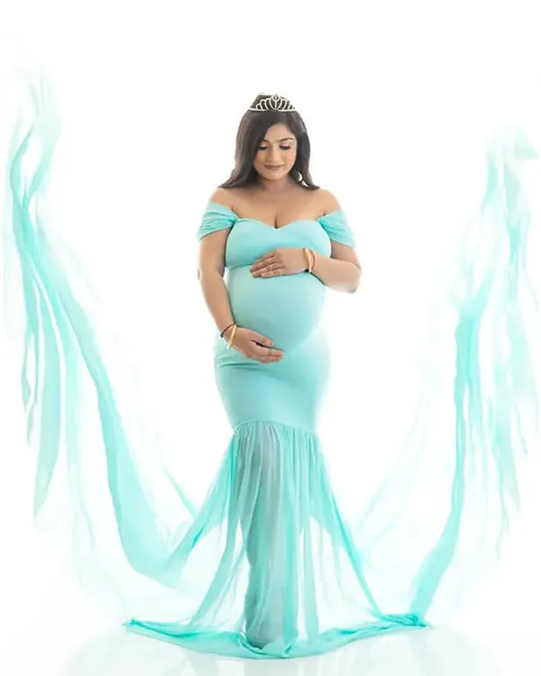 A full-length portrait of an expecting mother in a light blue gown, with flowing fabric creating a beautiful frame. The bright white background keeps the focus entirely on her.