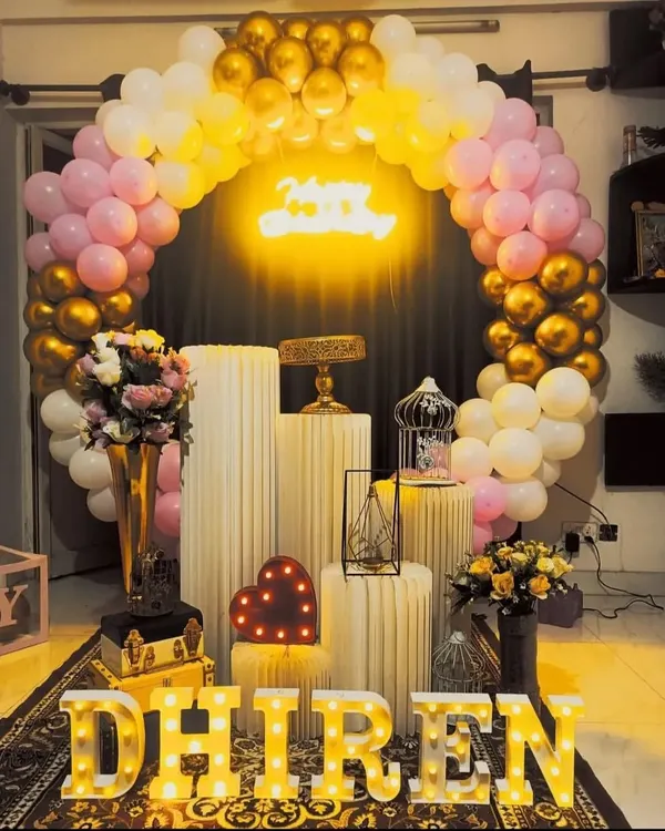 A beautiful birthday setup with a pink, white, and gold balloon arch. The arrangement of pedestals and props creates a balanced and elegant look.