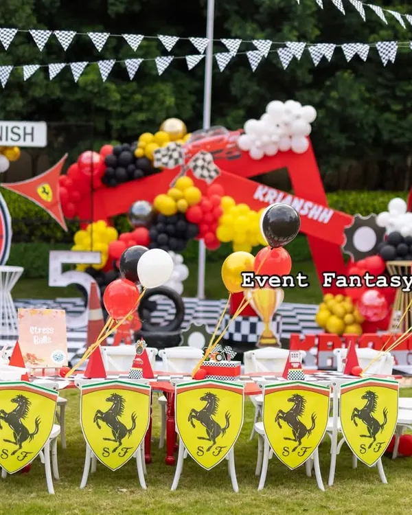 Welcome to the fast lane. This complete Ferrari-themed birthday setup features a custom circular backdrop with a speedometer, a kid-sized dining area with Ferrari shield chairs, and a full racing pit stop with a gas station prop and checkered flag details.