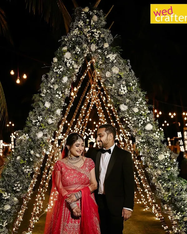 A fairytale entrance for a magical night. This couple is framed by a stunning floral teepee arch, illuminated by hundreds of fairy lights, setting a romantic tone for their beachside reception in Kerala.