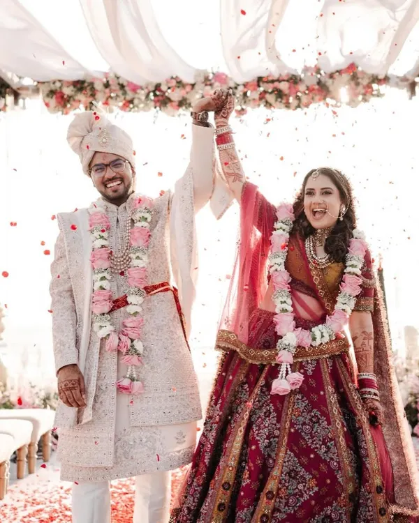 A perfect beach wedding moment. This happy couple celebrates under a canopy of flowing white fabric and pastel florals, with the beautiful Goa coastline in the background.