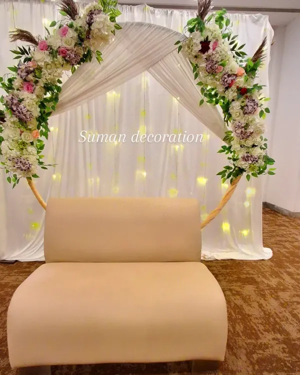 An elegant and romantic backdrop for a bridal shower or engagement. A circular gold frame is decorated with beautiful artificial flowers and greenery, set against a white curtain with fairy lights.