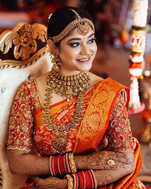 A classic South Indian bride in all her glory. This look features a stunning red and orange Kanjeevaram silk saree, paired with a heavily embroidered blouse and traditional temple jewelry for the main wedding ceremony.