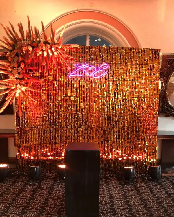 A glamorous photo booth featuring a golden sequin backdrop that shimmers in the light. We added a personalized neon sign with the couple's initials and a dramatic floral accent for a truly custom look.