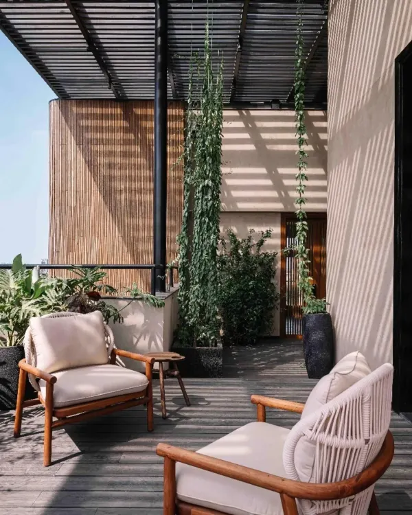 A cozy seating area on a wooden deck at Project 1374. The space is sheltered by a pergola and surrounded by vertical gardens, creating a private oasis that feels both indoors and outdoors.