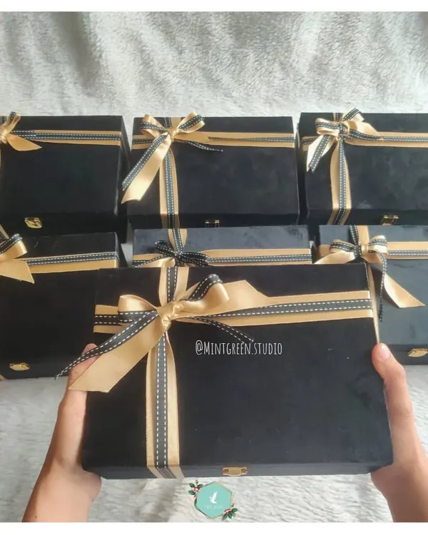A fleet of elegant black suede boxes ready for a corporate order. Each box is tied with a gold and black ribbon, ready to be filled with curated items that show genuine employee appreciation.