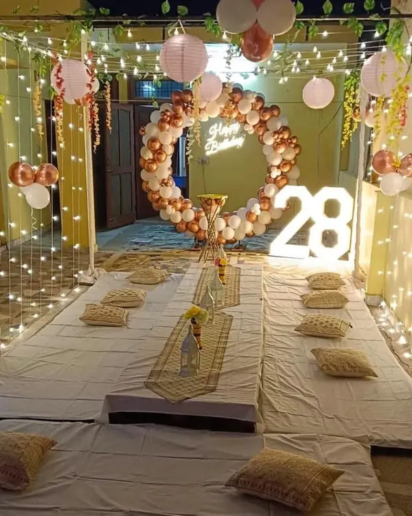 I can transform any space, like this terrace, into a cozy and magical party setting. This setup features a low seating arrangement under a canopy of fairy lights, a custom neon sign, marquee numbers for the age, and a beautiful balloon ring, perfect for a memorable 28th birthday celebration.