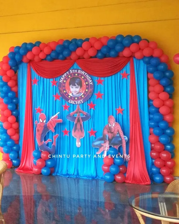 A classic Spiderman theme stage for a 5th birthday, featuring a vibrant red and blue balloon arch, character cutouts, and a personalized backdrop.