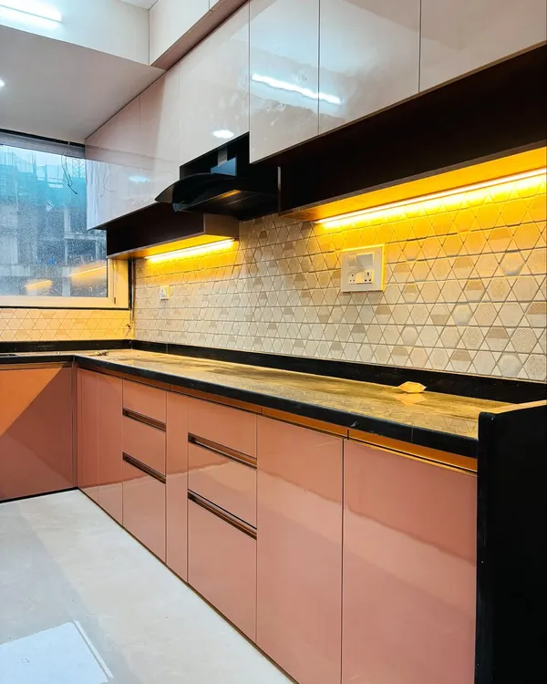 A modern L-shaped kitchen with glossy pink base cabinets and white overhead units. The geometric backsplash tiles and under-cabinet lighting create a bright and inviting cooking space.