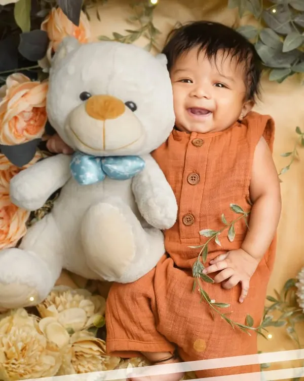 The happiest 3-month-old. This little boy's big smile, captured during his milestone session, is absolutely infectious. He's surrounded by flowers and cuddling his favorite teddy bear.